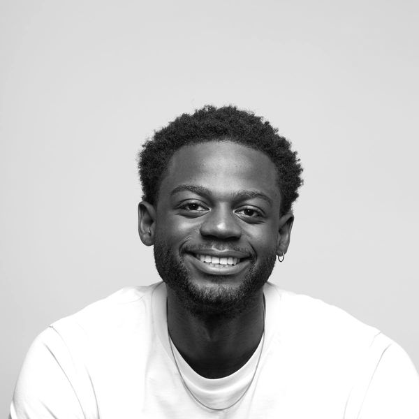 Smiling man wearing a white T-shirt with "LIMBA" logo, necklace, and earring, against a neutral background.