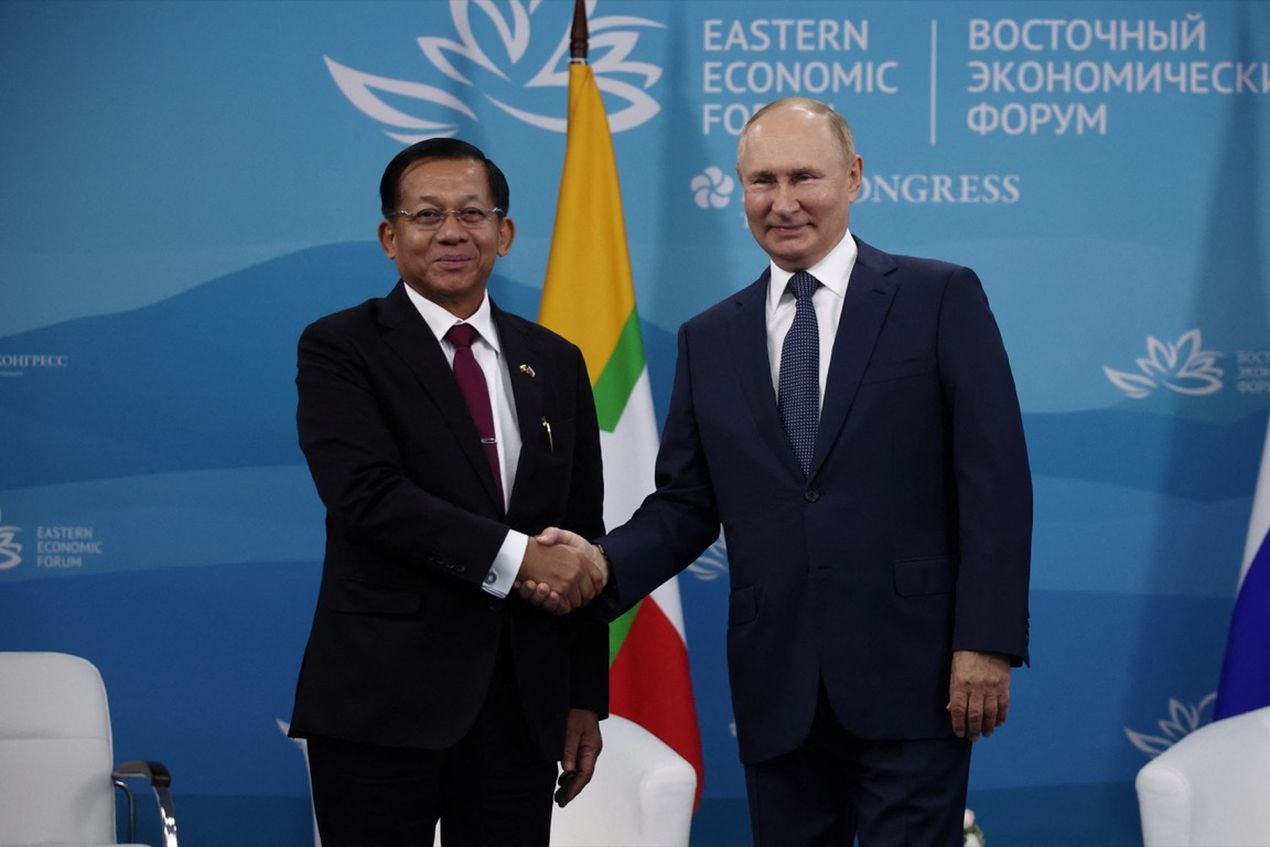 Two men in suits shaking hands at the Eastern Economic Forum, with flags and a blue backdrop displaying the event logo.
