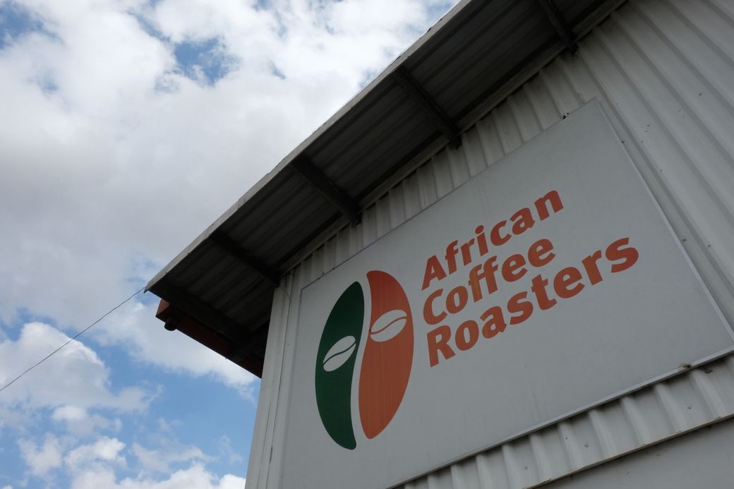 Building exterior with a sign reading "African Coffee Roasters" against a cloudy sky.