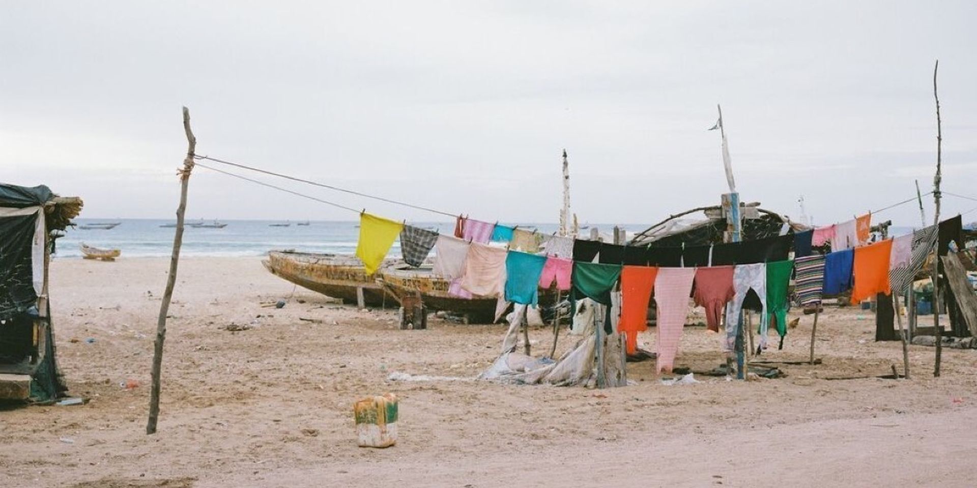 Colorful clothes hanging on a line at a sandy beach, with old boats and the ocean in the background.