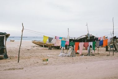 Colorful clothes hanging on a line at a sandy beach, with old boats and the ocean in the background.