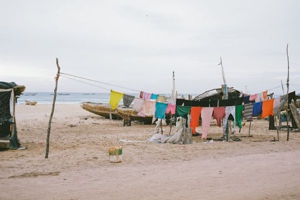 Colorful clothes hanging on a line at a sandy beach, with old boats and the ocean in the background.