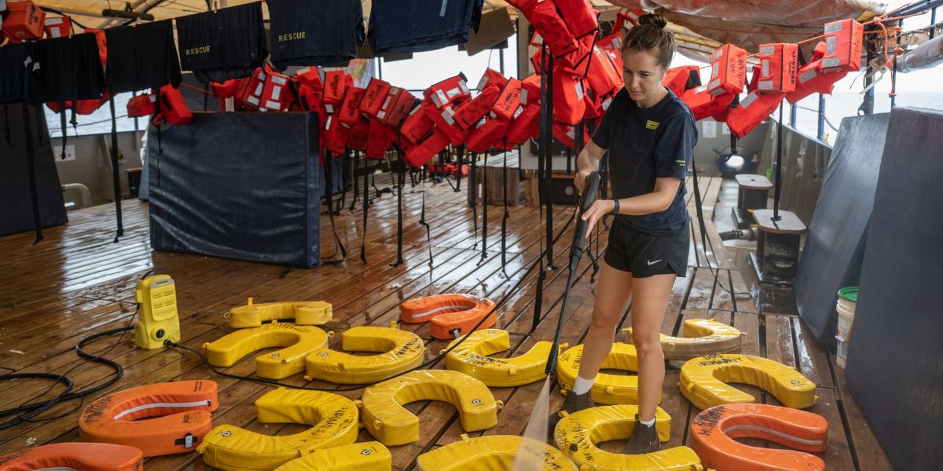 Een bemanningslid van reddingsschip Humanity 1 spuit reddingsvesten die op het dek liggen schoon.