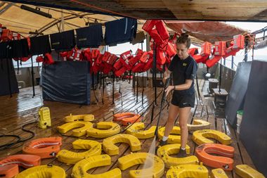 Een bemanningslid van reddingsschip Humanity 1 spuit reddingsvesten die op het dek liggen schoon.