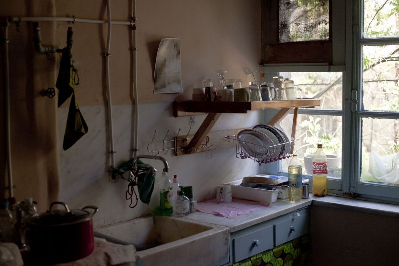 Een keuken in een van de gekraakte woonblokkken in Prosfygika. Je ziet een oude gootsteen, keukenkastjes, open waterleidingen tegen de muur.