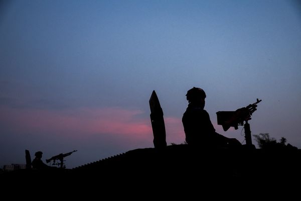 Silhouette of two soldiers on an armored vehicle at dusk, set against a sky transitioning from pink to blue.