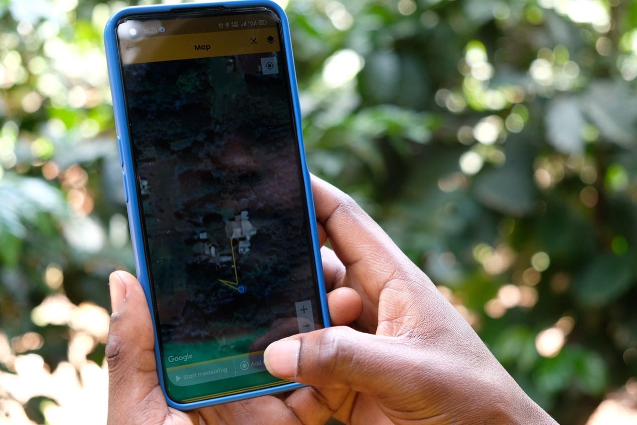 Hands holding a smartphone displaying a satellite map with a navigation line, surrounded by blurred greenery.