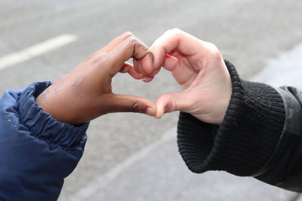 Een kinderhand en een hand van een jonge vrijwilliger vormen samen een hartje.