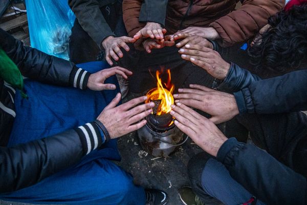 People gather around a small open fire outdoors, warming their hands in the cold.