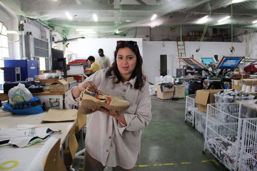 Top Manta-medewerkster Mariam poseert in het textielatelier met een paar sportschoenen van het eigen merk.