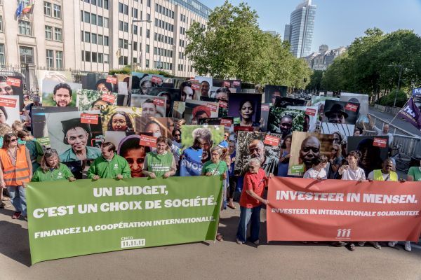 People holding large portraits and banners advocating for international cooperation in a demonstration outside modern buildings.