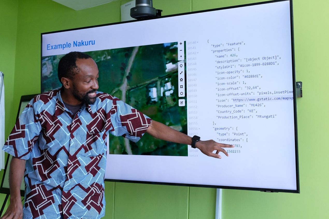 Man smiling and pointing at code and map on a screen labeled "Example Nakuru."