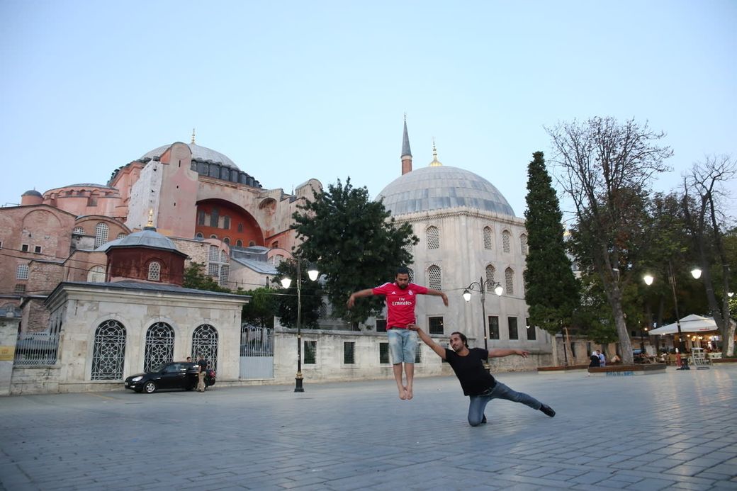 Two people pose playfully, one appearing to jump, in front of Hagia Sophia in Istanbul, during daylight.
