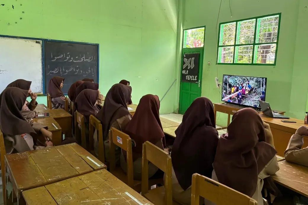 Gesluierde scholieren kijken naar een televisiescherm waarop de documentaire Pesta Babi wordt getoond.