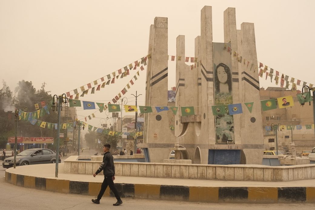 A man walks past a monument in a dusty street adorned with colorful flags and banners.
