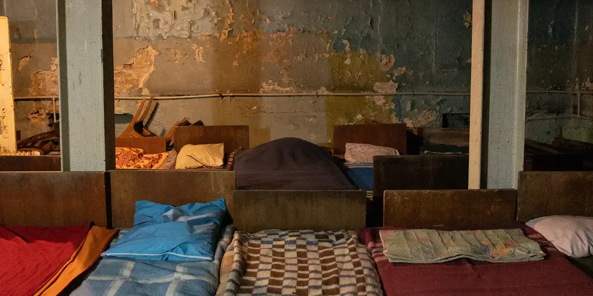 Gammele bedden met verschillende kleurrijke dekens in een ondergrondse schuilplaats