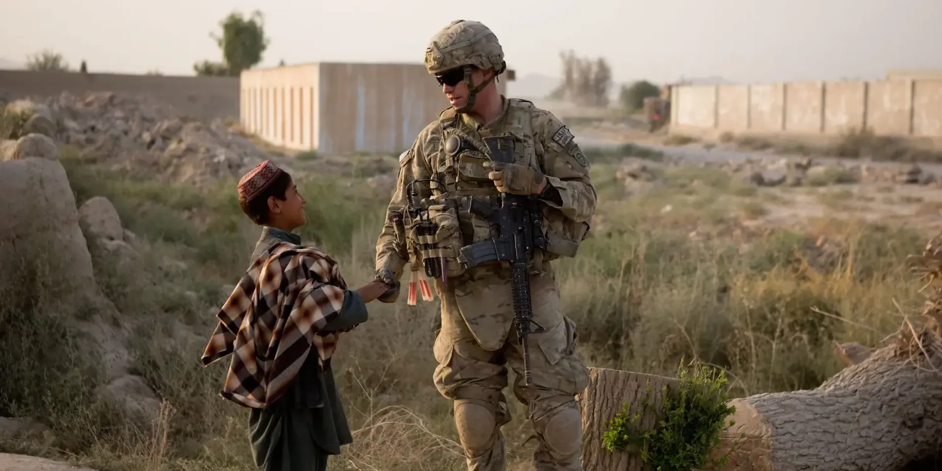 Kandahar, 2012. Een Afghaanse jongen en een Amerikaanse militair, die USAID-werknemers begeleidde bij hun bezoek aan een school in opbouw.
