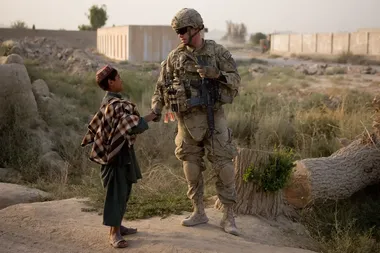 Kandahar, 2012. Een Afghaanse jongen en een Amerikaanse militair, die USAID-werknemers begeleidde bij hun bezoek aan een school in opbouw.