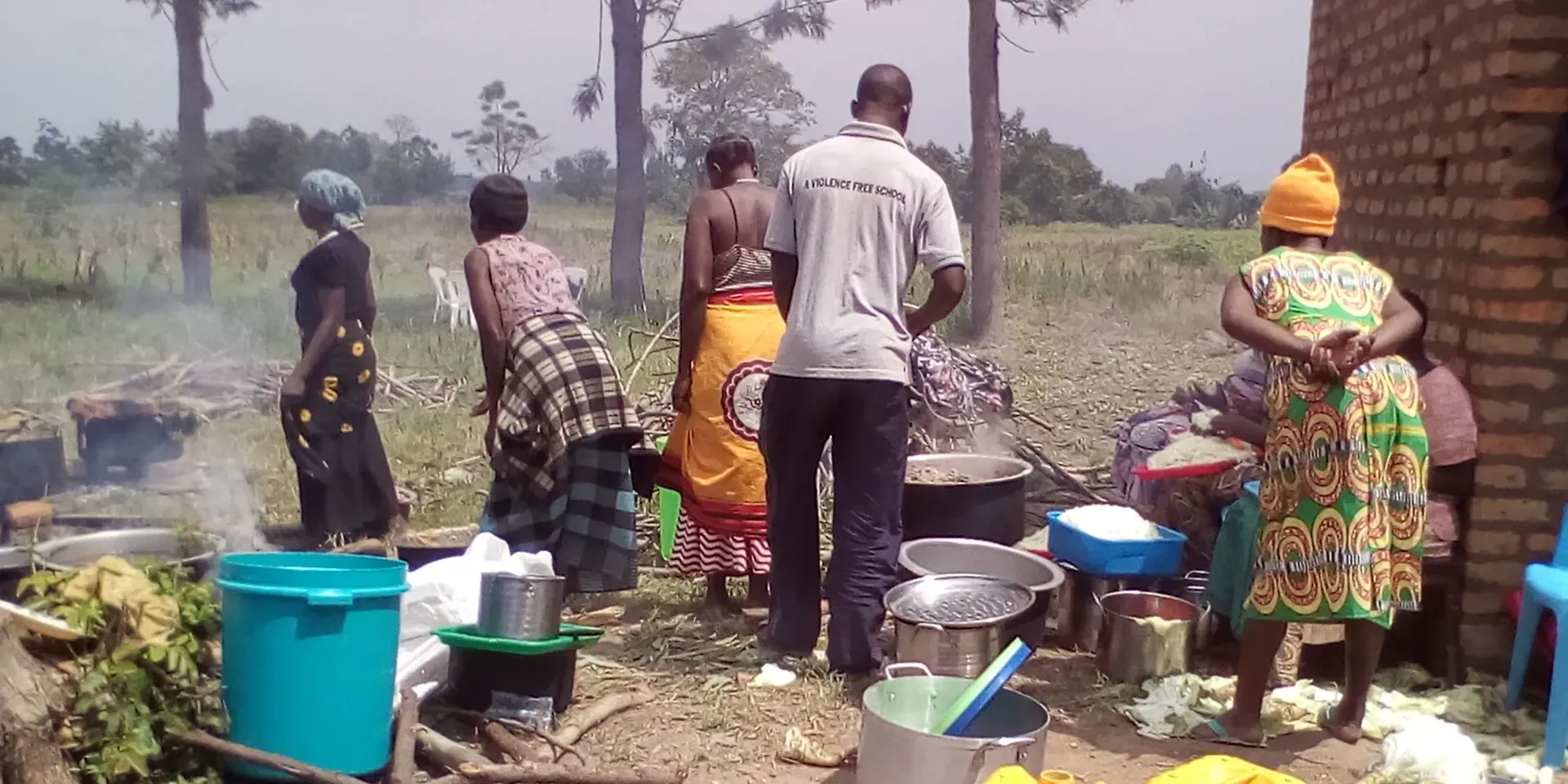 Afrikaanse vrouwen en een man bereiden maaltijden voor in grote potten op houtvuren.