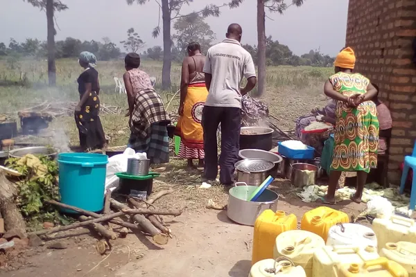 Afrikaanse vrouwen en een man bereiden maaltijden voor in grote potten op houtvuren.
