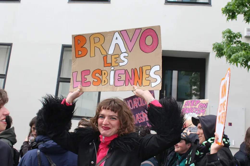 Een jonge vrouw houdt een pancarfte boven haar hoofd met de tekst ‘Bravo les lesbiennes’