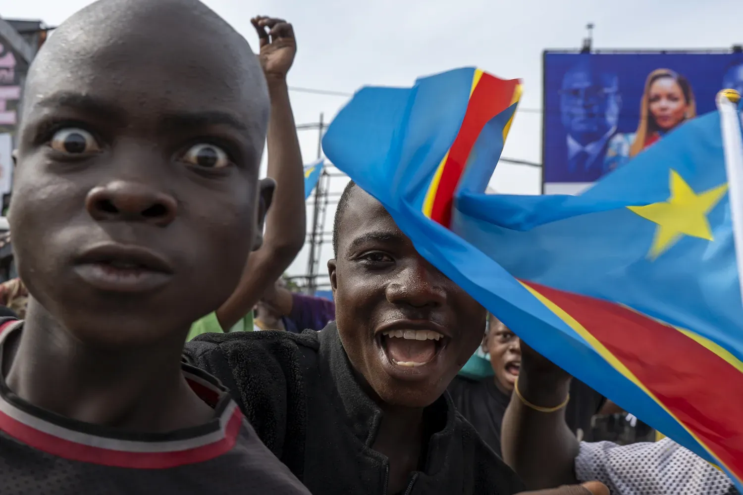 twee jongeren kijken en staren naar de cameralens. om hen heen wappert een Congolese vlag