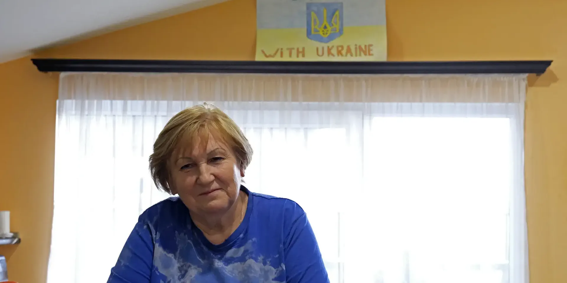 portretfoto van Russisch leerkracht Natalja Taranoesjenko aan een tafeltje met een tas koffie en voor een tekening met de tekst 'stand with Ukraine'