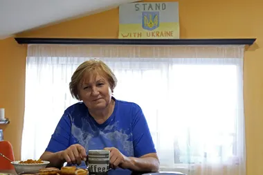 portretfoto van Russisch leerkracht Natalja Taranoesjenko aan een tafeltje met een tas koffie en voor een tekening met de tekst 'stand with Ukraine'