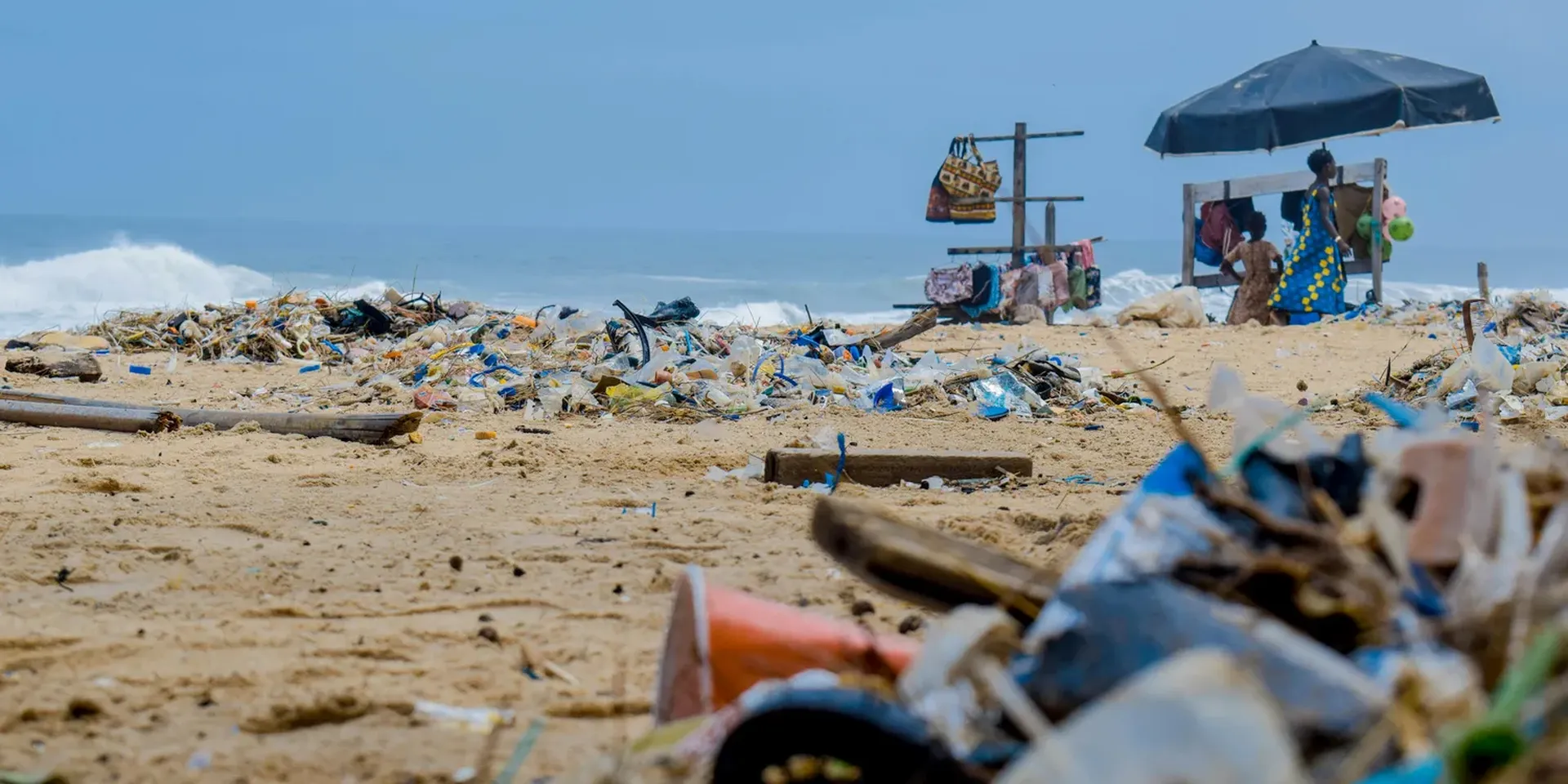 plastic afval op een strand. Op de achtergrond een verkoper onder een parasol