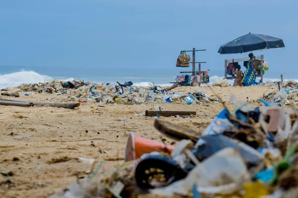 plastic afval op een strand. Op de achtergrond een verkoper onder een parasol