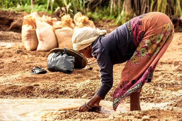 Een Afrikaanse vrouw staat gebukt voor eeen plas en zeeft goudhoudend erts in een illegale mijn.