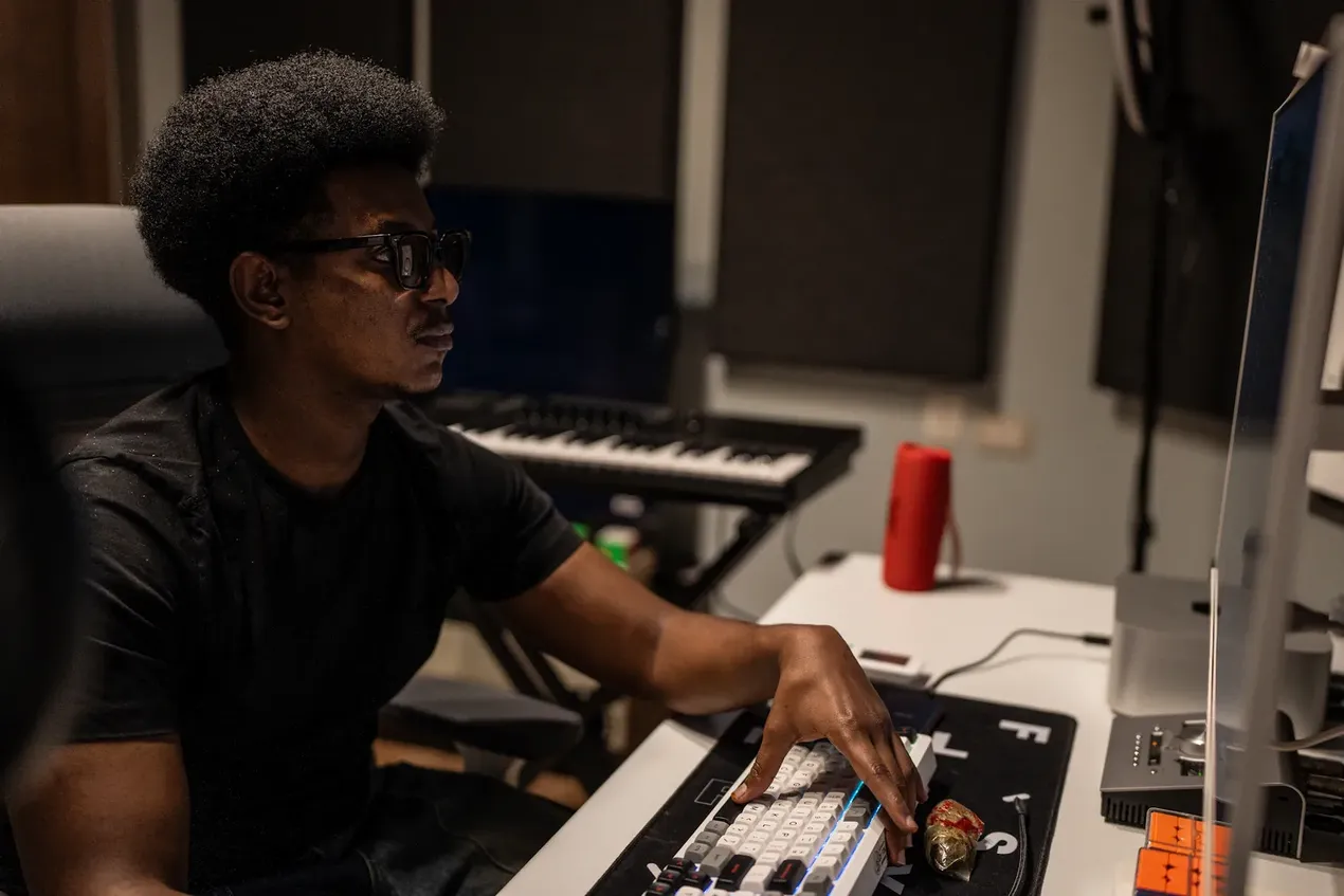 Beeld van een man (de Soedanese rapper Essam Satti) die naar een scherm kijkt. Op de achtergrondf staat een elektrich klavier.