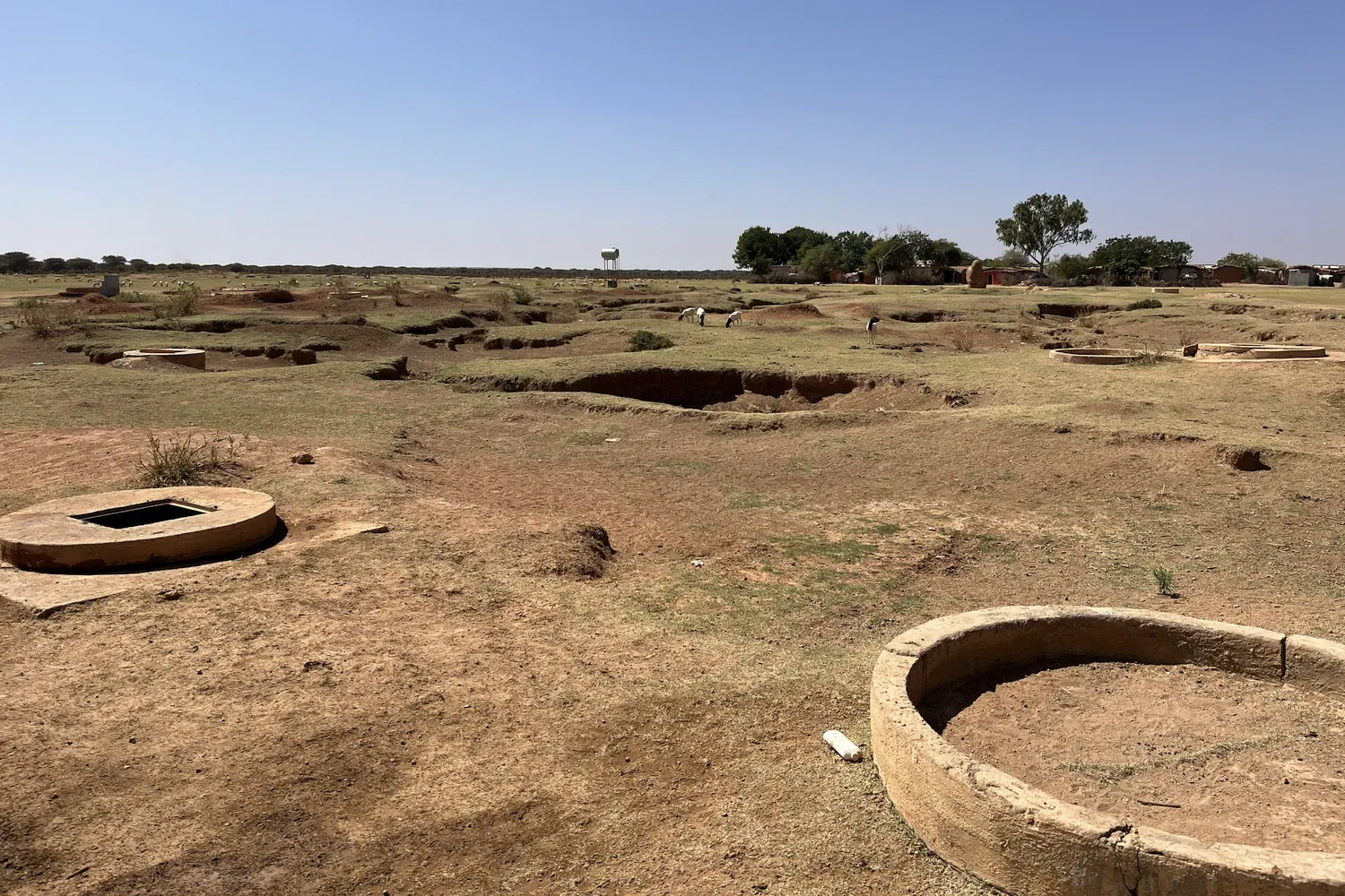 wijds uitzich op een schaars begroeide open vlakte. Op de voorgrond enkele waterputten