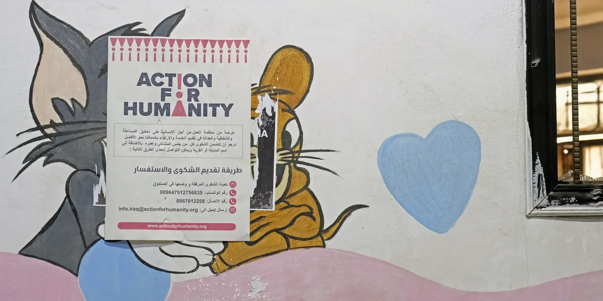 Muurschildering van Tom & Jerry overplakt met een affiche van Action for Humanity