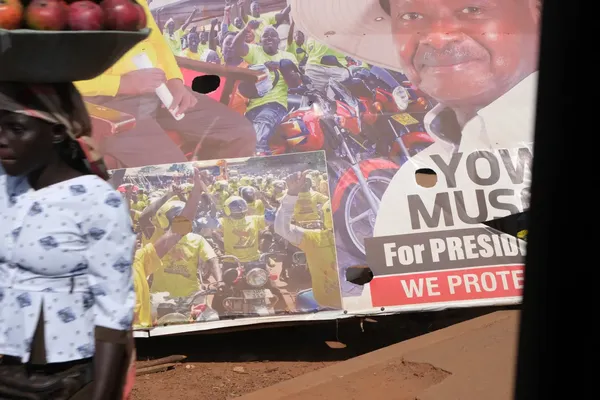 Een verkiezingsaffiche met daarop een portretbeeld van president Museveni en aanhangers in gele t-shirts op brommers