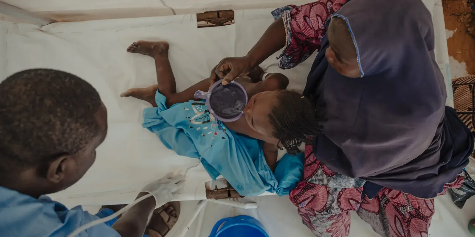 Een kind met cholera krijgt iets te drinken van haar moeder terwijl een verpleger toekijkt.