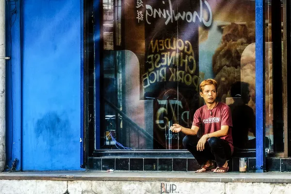 Een jonge man rookt een sigaret, gezeten voor een vitrine