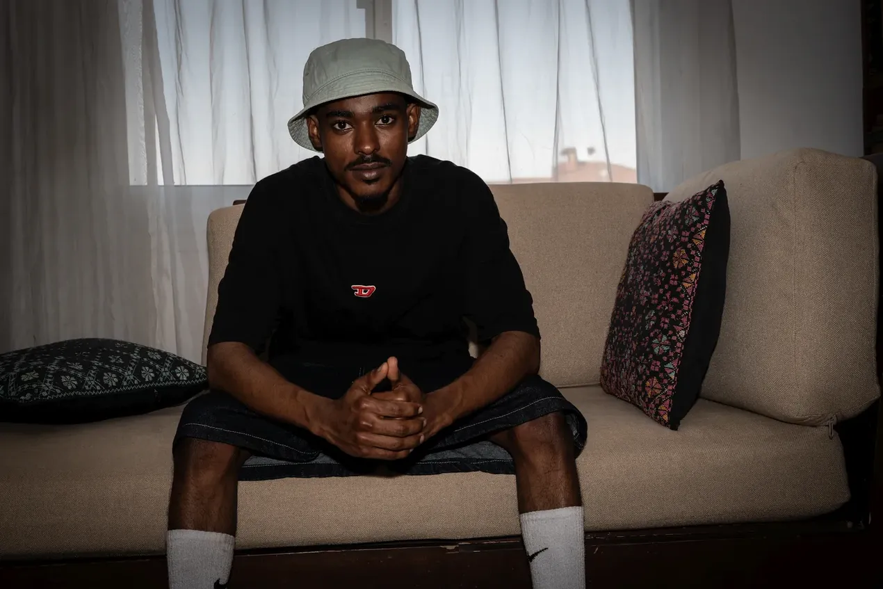 Een rapper (Hyper) zit in de zetel en kijkt naar de camera