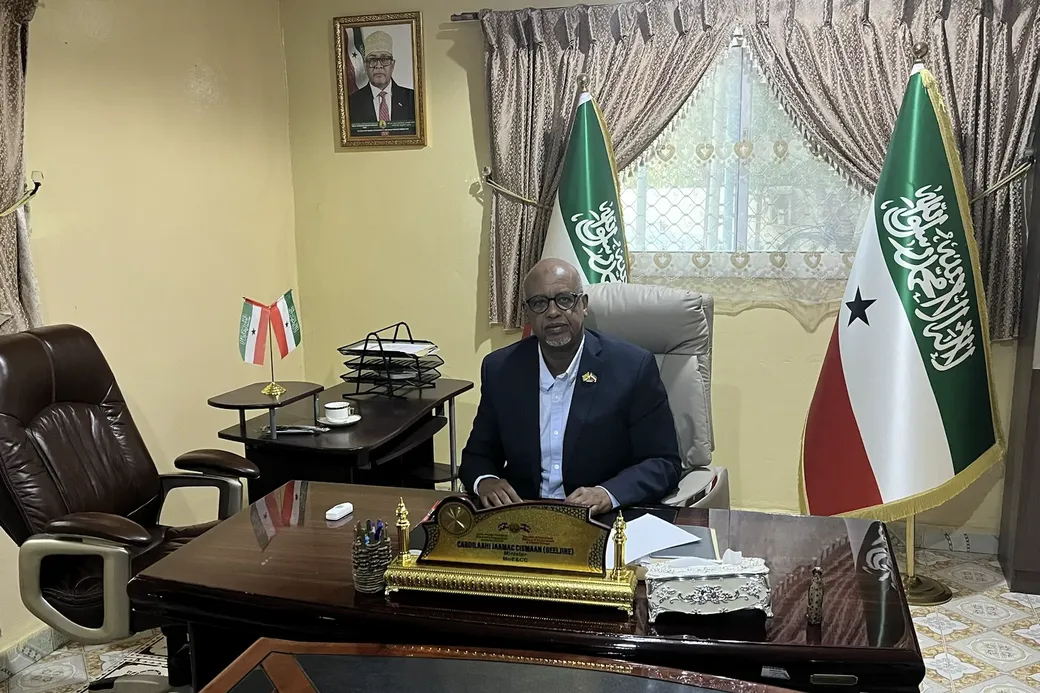 Een man zit aan zijn bureau. Achter hem twee vlaggen van Somaliland