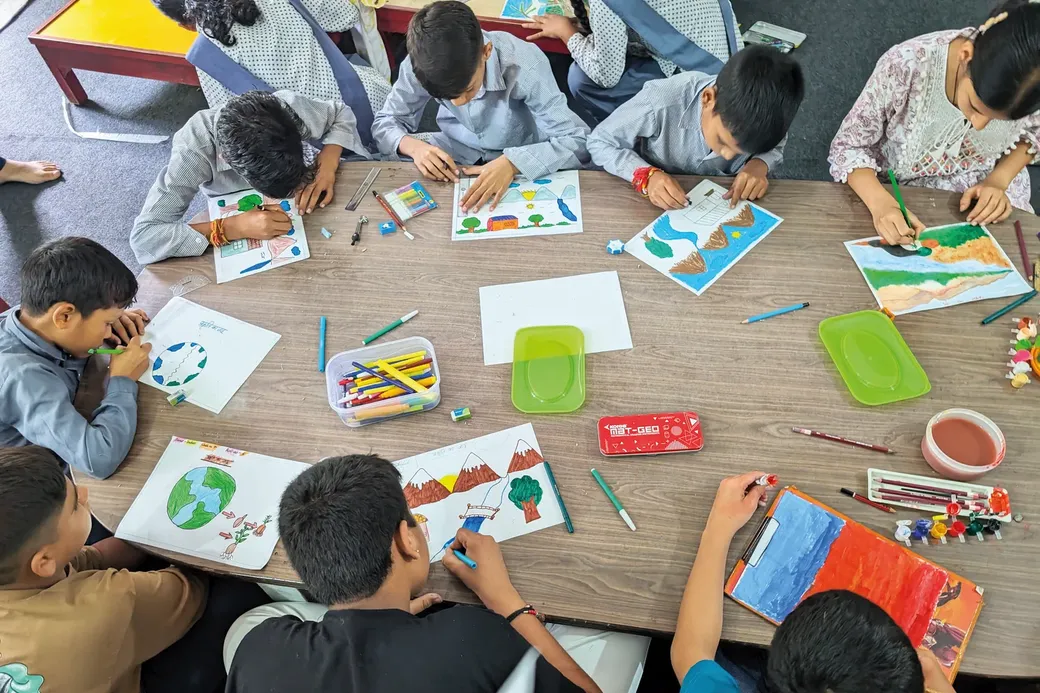 kinderen zitten rond een tafel en maken tekeningen op een blad papier