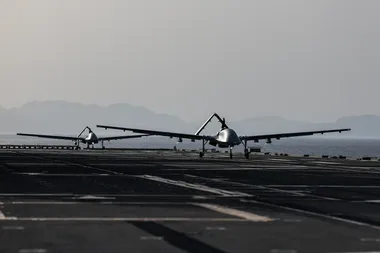 Twee grote drones staan achter elkaar op de startbaan van een vliegdekschip
