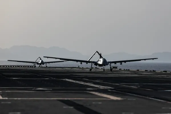 Twee grote drones staan achter elkaar op de startbaan van een vliegdekschip