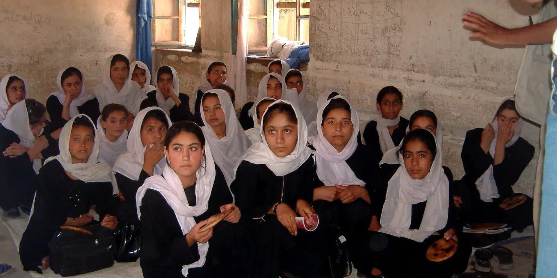 Afghaanse meisjes in zwarte kledij met een witte hoofddoek zitten samen in een klas (foto uit 2011)
