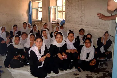 Afghaanse meisjes in zwarte kledij met een witte hoofddoek zitten samen in een klas (foto uit 2011)