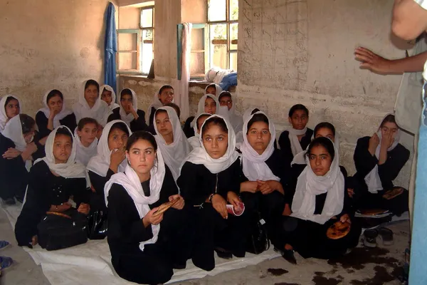 Afghaanse meisjes in zwarte kledij met een witte hoofddoek zitten samen in een klas (foto uit 2011)