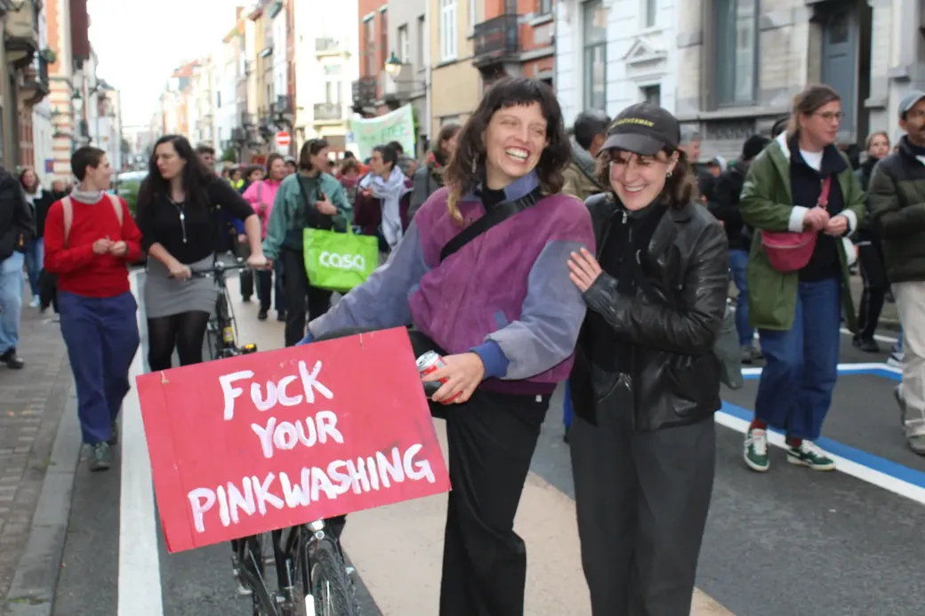 Twee vrouwen poseren bij een pancarte met de tekst ‘Fuck your Pinkwashing’