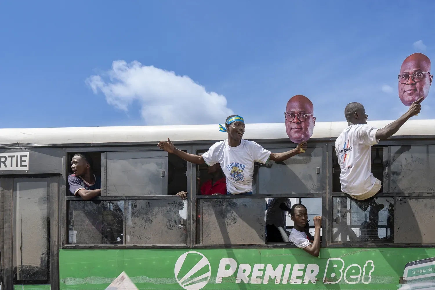 supoporters van Tshisekedi houden een foto van zijn hoofd vast terwijl ze half uit een bus hangen