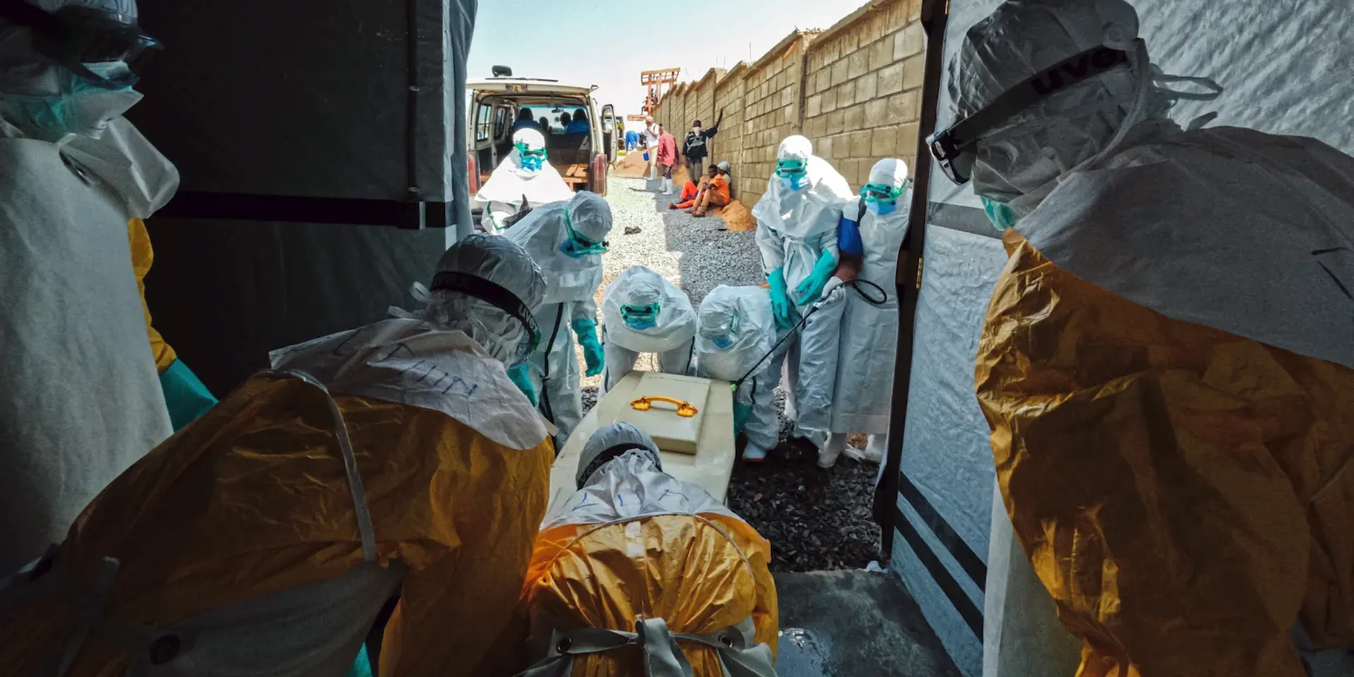 Hulpverleners in beschermende kledij dragen een doodskist naar buiten om het lichaam van een aan ebola overleden patiënt te begraven.