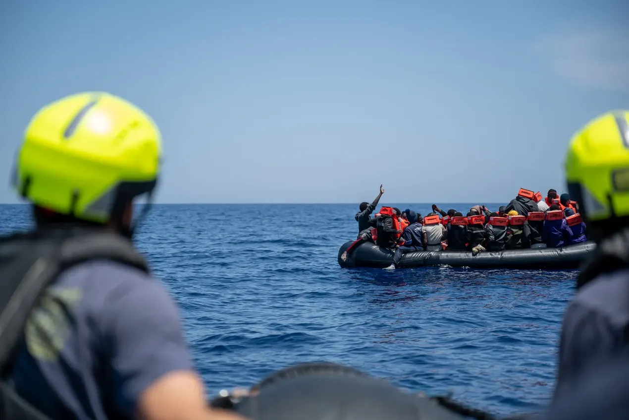 Twee redders op zee kijken naar een met mensen overladen rubberen sloep
