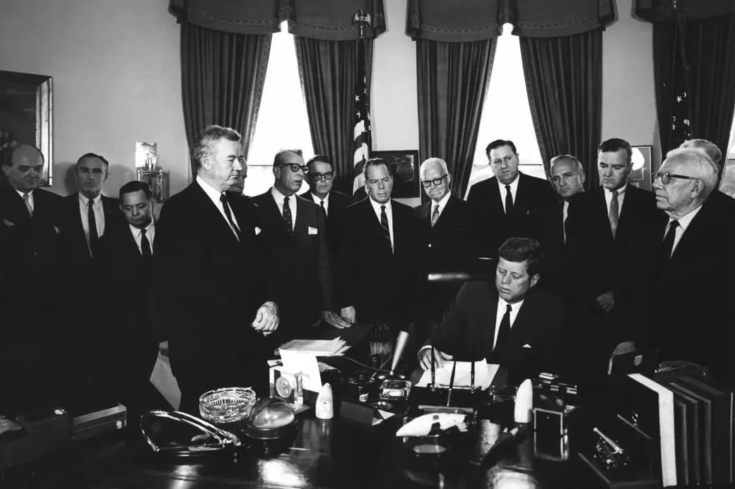 John F. Kennedy ondertekent de Foreign Assistance Act, begin jaren ʻ60, die leidt tot de oprichting van USAID.